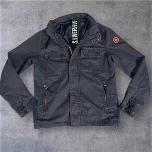 Mörkblå overshirt  från S.Oliver - Snygg mörkblå vindjacka från S.Oliver Urban Venture Gear 🌌 med ett coolt emblem på ärmen ✨. Jackan har flera praktiska fickor med dragkedja och knappar 🧥, hög krage 🏔️ och justerbara ärmslut 👌. Perfekt för dig som gillar streetstyle och funktionella detaljer 😎. 📦 Skickas samma dag som beställning. 💬 DM vid frågor!