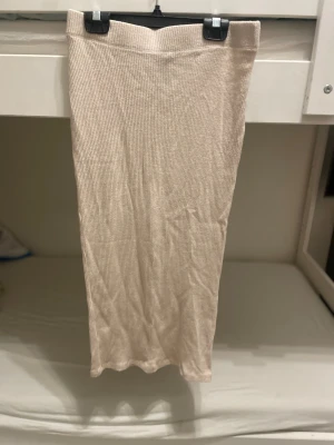 Beige ribbad långkjol från Gina Tricot - Säljer en beige långkjol från Gina Tricot i storlek S. Kjolen är ribbad och har en rak, slim passform som sitter snyggt längs kroppen. Materialet är mjukt och stretchigt, perfekt för en chill och stilren look. Enkel att matcha med både sneakers och boots.