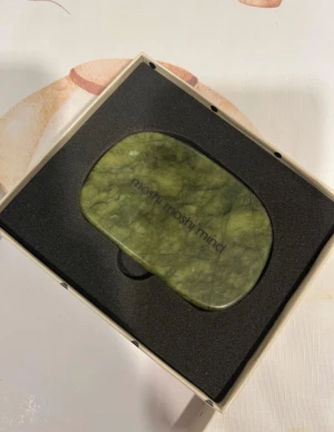 Grön Gua Sha-sten från Moshi Moshi Mind - HELT NY! Endast öppnad! Säljer en snygg Gua Sha-sten i grön jade från Moshi Moshi Mind. Perfekt för ansiktsmassage och för att boosta blodcirkulationen. Kommer i originalförpackning med svart skyddsinlägg. Stenen har en mjukt rundad form och känns lyxig och trendig.