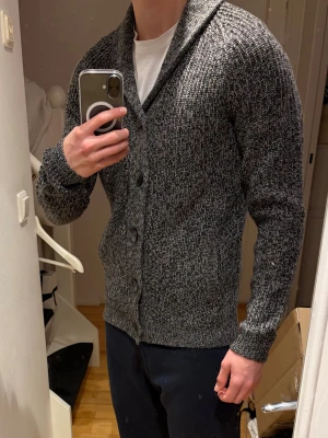 Grå cardigan - Säljer en sjukt fräsch gråmelerad kofta i storlek S. Koftan är stickad med grovt garn, har bred krage och fem stora svarta knappar framtill. Långärmad och med ribbade muddar vid ärmslut och nederkant. Perfekt för dig som gillar chill och stilren look. Han på bilden är 178 cm😇