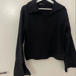 Svart stickad tröja med krage Gina Tricot - Svart stickad tröja från Gina Tricot i storlek XS. Tröjan har bred ribbad krage, v-ringad hals och långa ärmar med ribbade muddar. Modellen är loose fit och har en lite croppad passform. Perfekt för dig som gillar stilrena och bekväma plagg.