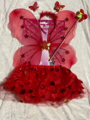 Röd glittrig kortkjol och Fjäril Vingar i 4 delar  - Säljer en röd kortkjol med glittriga paljetter och prickar, perfekt för att sticka ut på maskeraden eller temafesten. Kjolen är gjord i ett lätt och glansigt syntetmaterial som ger en cool volym. Matcha med vingar och trollspö för en magisk look! 3 år +  .   skicka med PostNord, inte instanbox 