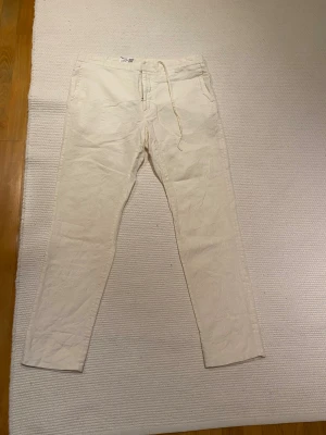 Vita linnebyxor från J.Lindeberg - Snygga vita linnebyxor från J.Lindeberg med rak passform och snörning i midjan. Byxorna har elastisk midja, sidofickor och en bakficka. 