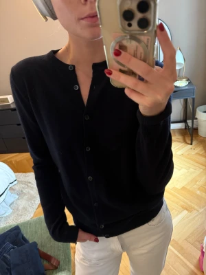 Mörkblå kashmirkofta - En klassisk mörkblå kofta i 100% kashmir med rund halsringning och knäppning framtill. Långärmad och med ribbade muddar vid ärmslut och nederkant. Knappt använd, mycket bra skick. Nypris 1400kr