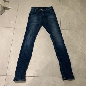 Mörkblå  jeans från Replay - Snygga mörkblå jeans från Replay med klassisk femficksdesign och diskreta slitningar. Jeansen har normal midja och är tillverkade i stretchigt denim för en bekväm passform. Perfekta för dig som gillar en smal siluett och stilren look.