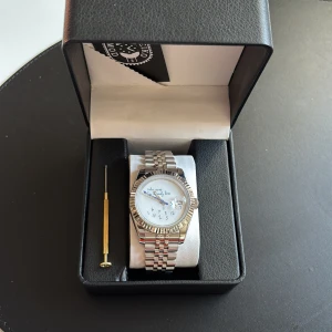 ”Who cares I’m already late” - Seiko automatisk klocka  - Säljer en stilren automatisk klocka från Seiko  Mod med silverfärgad länkarmband och boett. Urtavlan är vit med texten 'Who cares I'm already late' och har en klassisk rund form. Baksidan har ett transparent fönster som visar urverket. Säljer den då jag tyvärr inte kände att det var min stil. Klockan är helt ny och oanvänd. 