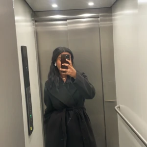 Svart kappa med bälte och bred krage - Stilren svart kappa med bred krage och knytbälte i midjan. Långärmad modell i klassisk design, perfekt för dig som gillar en clean och tidlös look. Materialet är mjukt och ger en lyxig känsla. Priset kan diskuteras💗