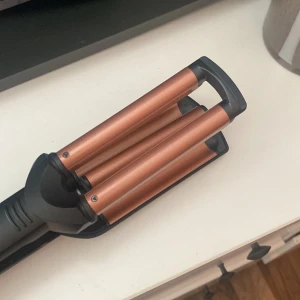 Vågtång från BaByliss - Stilren trippeltång för att skapa vackra vågor i håret. Kopparfärgade värmeplattor, justerbar värme och ergonomiskt handtag. Ser ut att vara i mycket gott skick utan synligt slitage. Perfekt för snabba och hållbara beach waves.