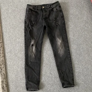 Svarta skinny jeans Kings Will Dream - Svarta jeans från Kings Will Dream med skinny passform och hög midja. Snygga slitningar och färgstänk på framsidan ger en cool, edgy vibe. Klassisk femficksmodell i stretchigt denim-material som sitter tajt och bekvämt.