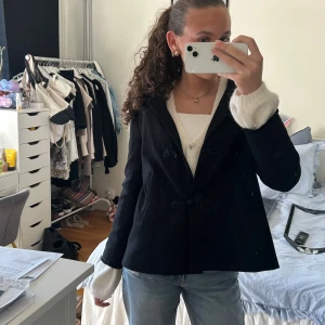 Svart kappa med dekorativa knappar - Säljer en svart kappa med snygga dekorativa knappar framtill och klassisk krage. Jackan har en rak passform och är i ett mjukt material som känns lyxigt. Perfekt för dig som vill ha en stilren och tidlös look. Aldrig använt 