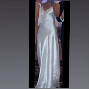 Vit långklänning med v-ringning - Säljer en elegant vit långklänning i satinliknande material med smala axelband och v-ringad hals. Klänningen har en figurnära passform och faller snyggt längs kroppen. Perfekt för dig som vill ha en stilren och lyxig look. Hade denna under balen, köpte den för 800kr säljer den för 450kr😊