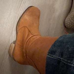 Bruna ofodrade kortare stövlar i skinn med dragkedja - Snygga bruna stövlar i äkta skinn med dragkedja på sidan och låg klack. Modellen har en fyrkantig tå och klassiska sömmar. Perfekt för dig som gillar stövlar med lite edge och naturlig look. Lite slitna framtill men går nog att putsa upp med färg. Stl: 39