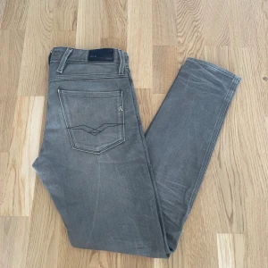 Grå Replay Anbass W30 L32 - Jag säljer dom här riktigt snygga Replay Anbass jeansen som är i storlek W30 L32. De är använda men fortfarande i fint skick utan skador. Tveka inte att höra av er!                                                     Mått: Längd 102cm. Midja 42cm