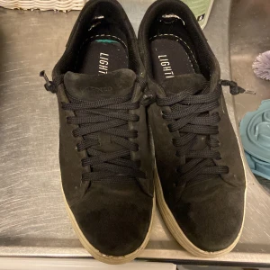 Svarta sneakers Selected Homme strl 43 - Ska tvätta dom! Svarta sneakers från Selected Homme i storlek 43. Skorna har en stilren design med svart mocka på ovansidan, svarta snören och en vit platt sula. Insidan har texten LIGHTMOTION. Perfekt för dig som gillar klassiska och enkla sneakers. Skickar med original sulan