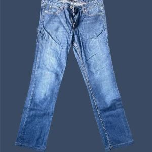 Blå straight fit Acne jeans - Snygga blå jeans med klassisk femficksdesign och raka ben. Jeansen har en ljus tvätt och kontrastsömmar samt en orange läderpatch bak i midjan. Perfekta för en avslappnad och stilren look.