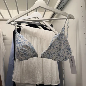 Vit och blå bikini från Gina Tricot - Supersöt bikiniöverdel från Gina Tricot i vitt med blått paisleymönster. Triangelformade kupor och tunna axelband med knyt. Perfekt för strandhäng och sommar vibes! Helt oanvänd med prislapp kvar.