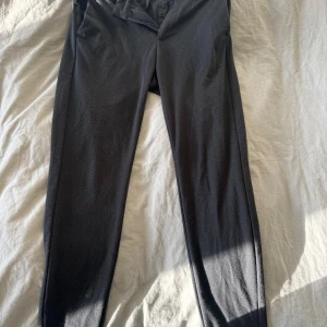 Svarta kostymbyxor Studio Total - Svarta kostymbyxor från Studio Total med smal passform och klassisk design. Byxorna har bälteshällor, dragkedja och knappstängning framtill. Materialet är mjukt och har en lätt stretch för extra komfort. Perfekta för en clean och stilren look.