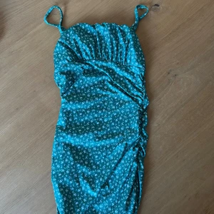 Turkos/grön blommig kort klänning - Snygg turkos kort klänning med smala axelband och små vita blommor. Använd 1 gång 