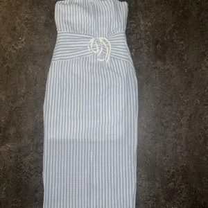 Blåvit randig bandeauklänning - Supersöt bandeauklänning i blåvitt randigt med knyt i midjan och slits bak. Lång modell som sitter snyggt och har en fräsch sommarkänsla. Aldrig använd, har storlek M men upplevde att den var för liten 