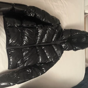 Svart glansig pufferjacka från Colmar - Snygg svart pufferjacka från Colmar med glansig finish och huva. Jackan har dragkedja framtill och klassisk Colmar-logga på ärmen. Perfekt för kalla dagar när du vill hålla stilen och värmen. Ny pris 4300kr köpt ifrån kidsbrandstore för cirka ett år sedan. Säljs för 2000kr men pris går att diskutera, har ett hål lite större än på bilden 💕liten fläck på inre armen som inte syns, uppskattas sitta som en xs möjligtvis mindre 