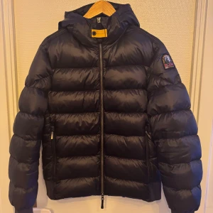 Svart dunjacka Parajumpers Sheen M - Säljer en svart dunjacka från Parajumpers, modell Sheen. Jackan har huva, dragkedja framtill och två sidofickor med dragkedja. Klassisk pufferstil med markerade sömmar och gul detalj vid halsen. Perfekt för kalla dagar och riktigt snygg streetstil. Köpt från NK och nypris ligger på 7500kr. Bara att skriva vid frågor och priset går såklart att diskutera!