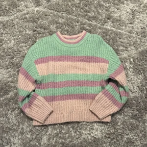Randig stickad tröja från Gina Tricot - Supermysig stickad tröja från Gina Tricot i storlek XS. Tröjan har breda pastellfärgade ränder i ljusgrön, ljusrosa och lila, samt ribbade muddar vid ärmslut och nederkant. Perfekt för sommaren eller hösten!😊