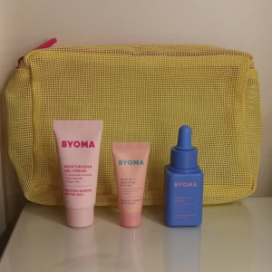 BYOMA hudvårdskit med necessär - Säljer ett BYOMA hudvårdskit med tre produkter: en rosa Moisturizing Gel-Cream, en ljusrosa De-Puff + Brighten Eye Gel och ett blått Hydrating Serum. Allt kommer i en gul mesh-necessär med rosa dragkedja. Perfekt för dig som vill boosta din hudbarriär. Ögonkrämen och den rosa krämen är helt nya, och serumet är lite använt men vet inte riktigt hur mycket det är kvar. Tror det är ca hälften kvar av det.