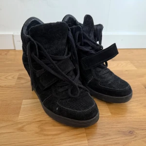 Svarta wedge sneakers från Limited - Säljer ett par svarta sneakers med inbyggd kilklack från Limited. Skorna är i mocka med snörning och kardborreband för extra cool look. De har en hög siluett och rund tå, perfekt för dig som vill ha både stil och höjd i vardagen.