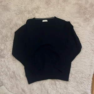 Mörkblå stickad tröja från MNG - En stilren mörkblå stickad tröja från MNG med v-ringad hals och ribbade muddar. Perfekt för lager-på-lager och funkar till jeans. Klassisk modell med lång ärm och mjukt material.