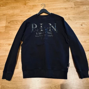 Svart sweatshirt från Philipp Plein - Svart sweatshirt från Philipp Plein med tryckt logga och text framtill. Tröjan har rund hals, långa ärmar och ribbade muddar vid ärmslut. Självklart äkta! Sparsamt använd. Storlek M. 