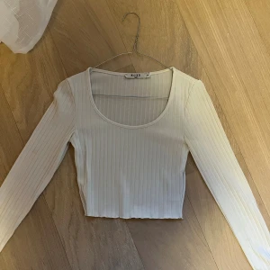 Vit ribbad topp från NA-KD - Säljer en vit ribbad topp från NA-KD med lång ärm och rundad urringning. Toppen är i stretchigt material och har en tajt passform. Storleken passar mig som har xs