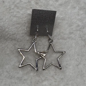 Silvriga stjärnörhängen - Coola örhängen i form av öppna stjärnor i silverfärgad metall. Perfekta för att ge din look lite extra edge och passar dig som gillar unika detaljer. Hängande modell som syns och sticker ut. Krokarna är i sterling silver 