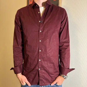 Vinröd Tiger of Sweden skjorta - Säljer denna stilrena vinröda skjorta från Tiger of Sweden i slim fit. Den är i riktigt fint skick och bara provad på. Tagg finns kvar på skjortan (Bild 3). Modellen är 181cm lång och väger 72, tveka inte vid frågor eller prisförslag🍷🧳!