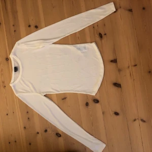 Vit långärmad tröja från Gina Tricot - En basic vit långärmad tröja från Gina Tricot i mjuk och tunn bomull. Tröjan har rund halsringning och en slim passform som sitter snyggt på kroppen. Perfekt att styla med jeans eller kjol för en clean look. Man ser bh under