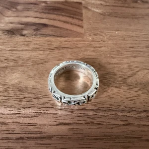 Chrome Hearts silverring med gravyr - Säljer en fet silverring från Chrome Hearts med snyggt, detaljerat mönster runt hela ringen. Insidan är graverad med märkets logga och årtal. Perfekt accessoar för dig som gillar statement-smycken och exklusiv streetstyle. Size 10.  Stainless steel