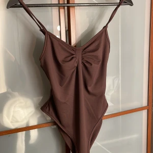 Brun body - Supersnygg brun body med smala axelband och rynkdetalj framtill. Modellen har högt skurna ben och en enkel, stilren look. 