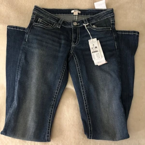 Mörkblå bootcut jeans från Gina Tricot 14+ - Mörkblå jeans från Gina Tricot 14+ i bootcut-modell i storlek M med snygga slitningar och kontrastsömmar. Bakfickan har ett broderat mönster i vitt och rosa. Jeansen har låg midja och klassisk femficksdesign. Jeansen är aldrig använda utan endast testade och säljs med prislapp kvar!!💗💗