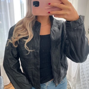 Svart skinnjacka i äkta läder - Snygg svart skinnjacka i äkta läder. Jackan har klassisk trendig bombermodell. Finns små defekter på jackan (se 2 sista bilderna, kontakta mig för fler bilder). Väldigt fint vintage-skick. Märkt strl 42 men passar mig som har strl S.