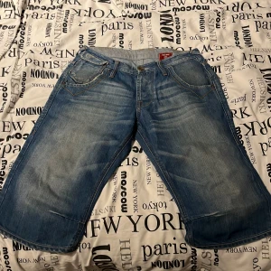 Blå jeansshorts från Jack & Jones - Säljer ett par blå jeansshorts från Jack & Jones med klassisk femficksdesign och snygga slitningar. Modellen är loose fit och har stora bakfickor med lock. Perfekta för en avslappnad stil under sommaren.