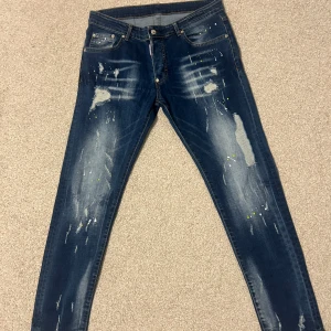 Dsquared2 skinny jeans med slitningar - Snygga blå skinny jeans från Dsquared2 med coola slitningar och färgstänk. Jeansen har klassisk femficksdesign, låg midja och är tillverkade i bomull med stretch. Perfekta för dig som gillar en edgy streetstil och vill sticka ut lite extra.
