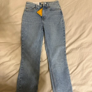  ljusblå  jeans - Klassiska jeans i ljusblå tvätt med raka ben och hög midja. Jeansen har bälteshällor och stängs med knappgylf. Perfekta för en avslappnad och tidlös look. aldrig använda, prislappen sitter kvar