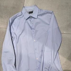Tiger Of Sweden skjorta - Snygg ljusblå skjorta från Tiger of Sweden i extra slim fit. Klassisk krage, långa ärmar och knappar framtill. Perfekt för dig som gillar stilrena och moderna plagg. Skjortan är gjord i mjuk bomull och har en clean look utan mönster och sticka ut med den fetaste outfiten i skolan eller på festen! Storleken är M och passar mig som är ungefär 185cm! Skicket är mittemellan då det finns ganska synliga tecken på kragen där den ”gulnat” ska testa och få bort det! Hör av dig vid minsta fråga mvh EM
