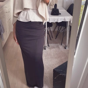 Grå långkjol med tight passform - Säljer en grå långkjol med tight och figurnära passform. Kjolen har en enkel och stilren design med detlaj på sidan, Materialet känns mjukt och följsamt mot kroppen.