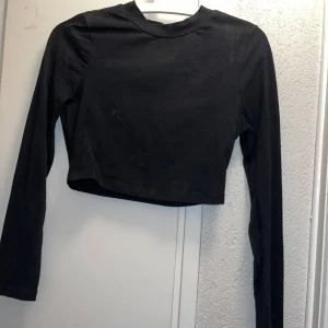 Svart croppad långärmad topp - En stilren svart croppad topp med lång ärm och rund hals. Tillverkad i mjuk bomull som känns skön mot huden. Enkel och clean design utan mönster eller detaljer, perfekt att matcha med dina favoritjeans eller kjol. Två fläckar som går bort I tvätten men har inte tiden själv 