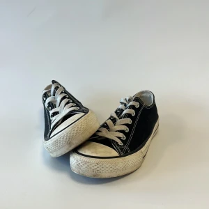 Svarta låga sneakers med vit sula - Klassiska svarta dam sneakers med vit gummisula och vita snören. Skorna har rund tå och kontrasterande vita sömmar som ger en cool retrovibe. Ovandelen är i canvas och sulan är platt med tydligt mönster. Perfekt för dig som gillar enkel och tidlös stil.