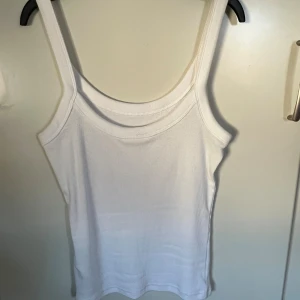 Vit ribbad linnetopp från Gina Tricot - Säljer en vit ribbad linnetopp från Gina Tricot, basically basics-kollektionen. Toppen har breda axelband och rundad halsringning, perfekt för en clean och enkel stil. Materialet är mjukt och stretchigt för en bekväm passform.