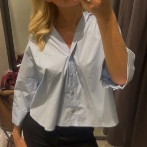 Ljusblå oversized skjorta med knappar - Säljer en ljusblå oversized skjorta med v-ringning och stora trekvartsärmar. Skjortan har knappar framtill och är tillverkad i ett tunt bomullstyg som ger en luftig känsla. Perfekt för dig som gillar en avslappnad och trendig stil.