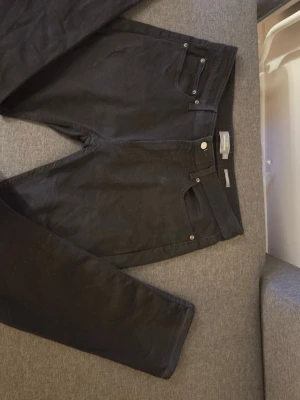 Svarta jeansbyxor från Dressmann - Svarta jeansbyxor från Dressmann i klassisk femficksmodell med raka ben och normal passform. Byxorna har bälteshällor, knapp och dragkedja framtill samt två bakfickor. Materialet är slitstarkt och bekvämt bomullstyg.