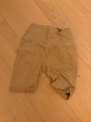 Beige höga träningsshorts Aim'n XS - Säljer ett par beige höga träningsshorts från Aim'n i storlek XS. De har en strukturerad yta och bred midja som sitter skönt. Materialet är en mix av polyamid, polyester och elastan vilket gör dem stretchiga och perfekta för gymmet eller löpning.