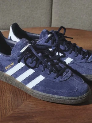 Adidas Spezial sneakers marinblå mocka - Adidas Spezial sneakers i marinblå mocka med ljusblå ränder på sidorna, gummisula och snörning. Ikonisk retrostil med guldfärgad Spezial-logga på sidan och klassisk rund tå. Perfekta för dig som gillar streetwear och snygga detaljer. Det är i bra skick och kommer även med kartongen. Storleken är 42, 2/3.